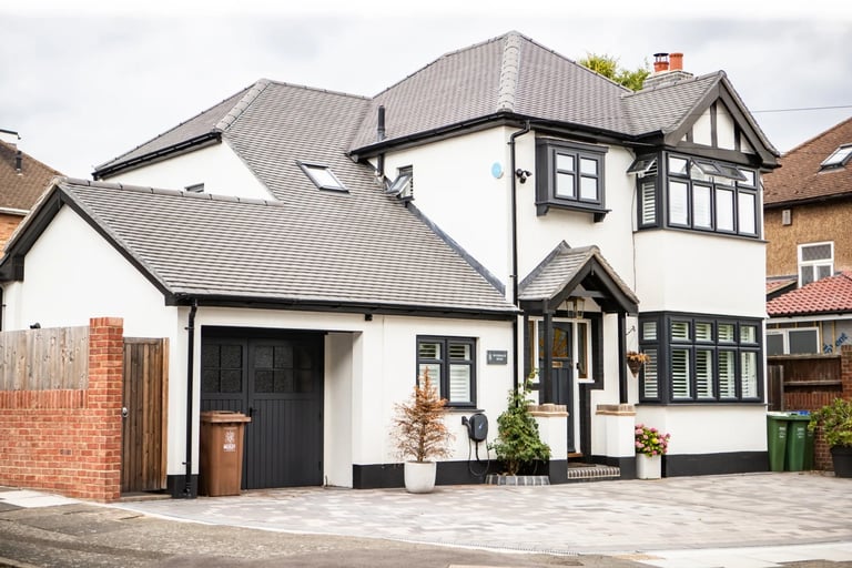 Modern two-story home with white and black exterior, dark roof, black garage door, and brick paver driveway