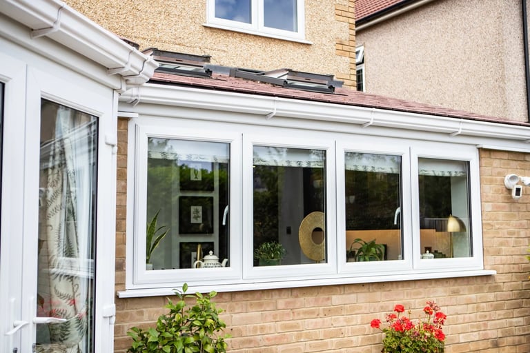 Modern white-framed conservatory extension on brick house with flowering shrubs in front garden