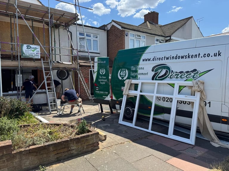Construction crew installing windows on brick house with white van and scaffolding visible
