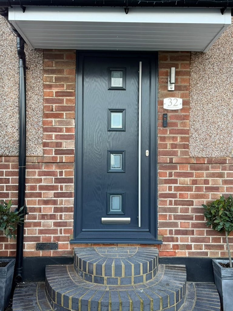 Modern dark blue front door with four small windows set in a red brick house entrance with curved brick steps and white overhang