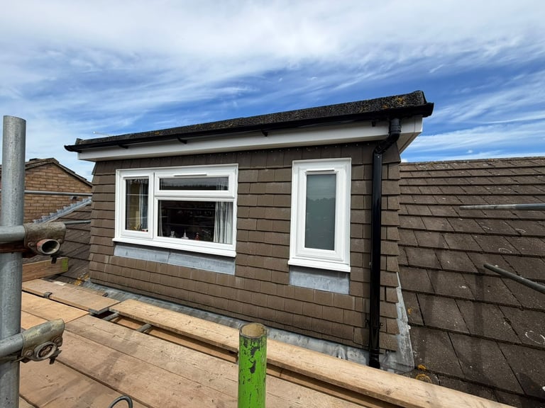 Rooftop cabin extension with dark wood siding, white-framed window and door, wooden deck, and blue sky with clouds