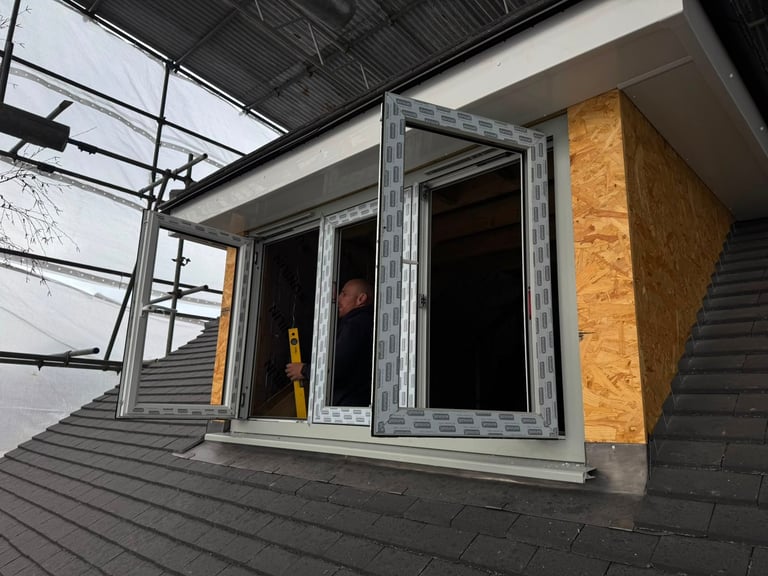 Exterior view of a residential building with large glass sliding doors and windows on corrugated metal siding, yellow insulation visible inside.