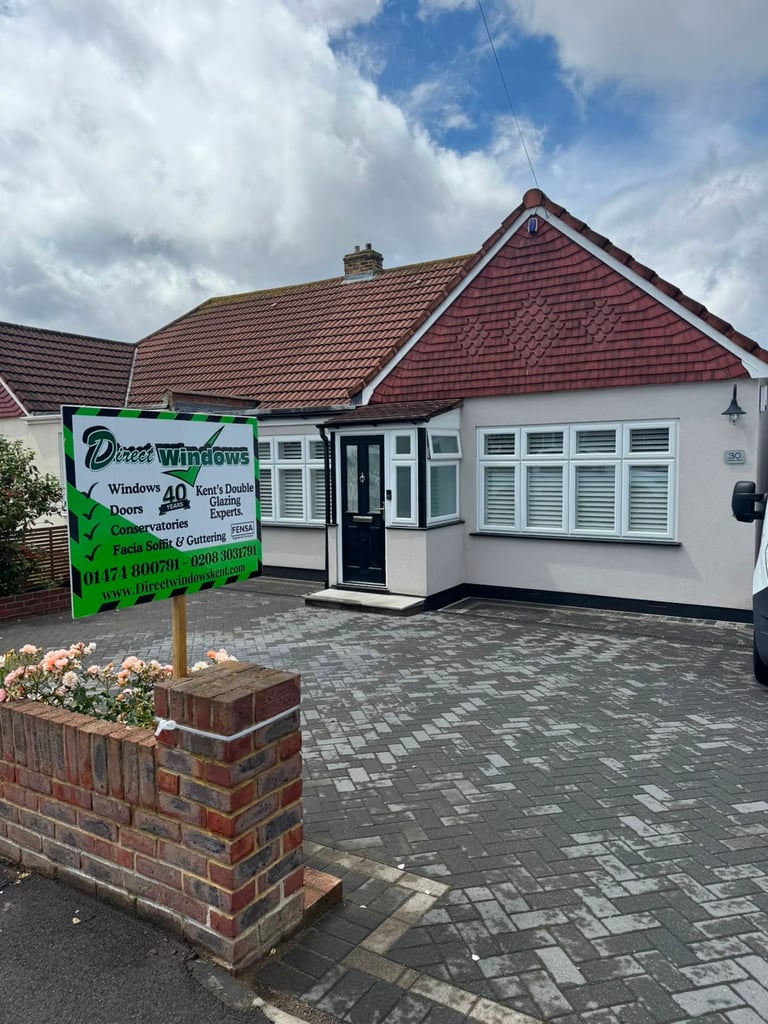 A bungalow with red roof and white exterior displays a green Doors Windows sign advertising home improvement services