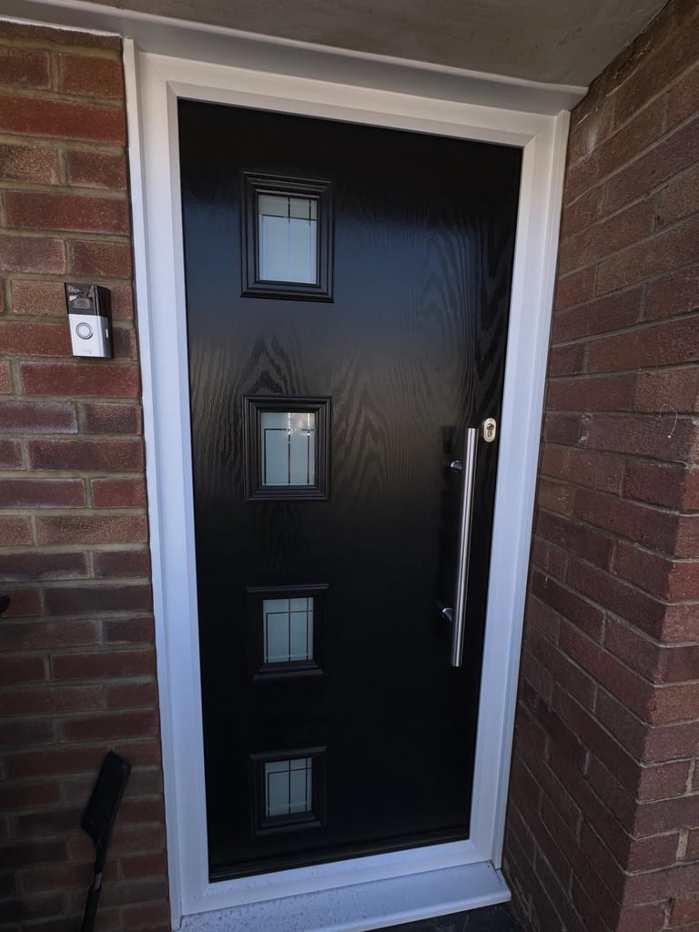Black front door with four small rectangular windows and chrome handle, set in white frame on brick house exterior