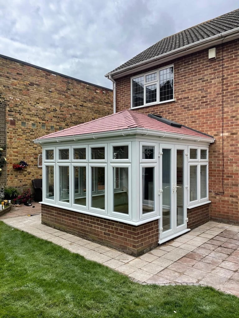Modern brick conservatory with pink roof and white frames attached to residential home, featuring landscaped garden and patio
