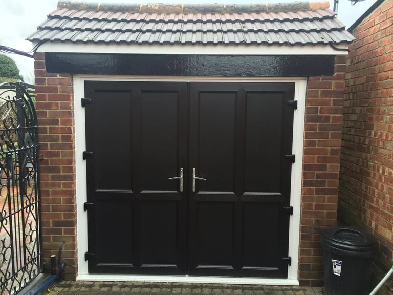 Black double garage doors with white frame on red brick house exterior