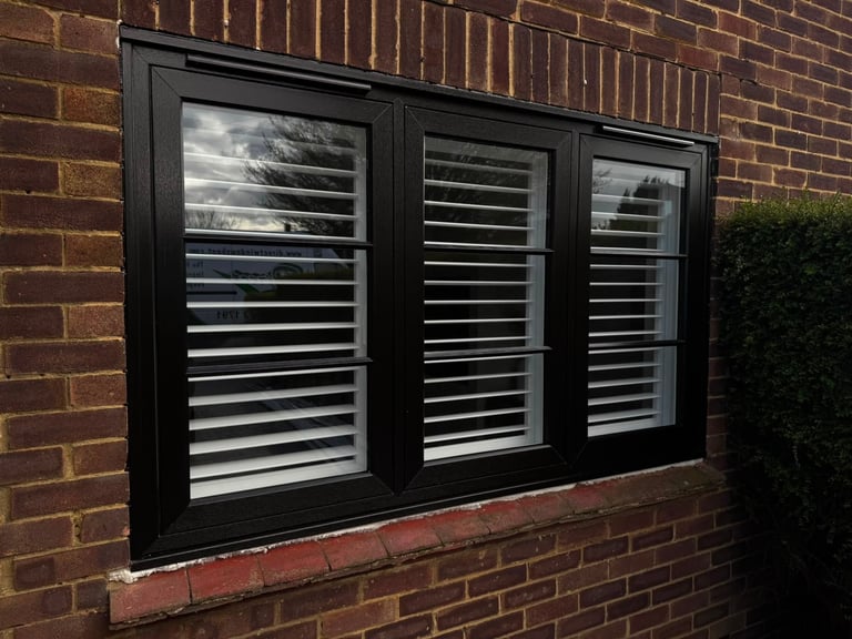 Black framed triple window with white horizontal blinds mounted on red brick wall