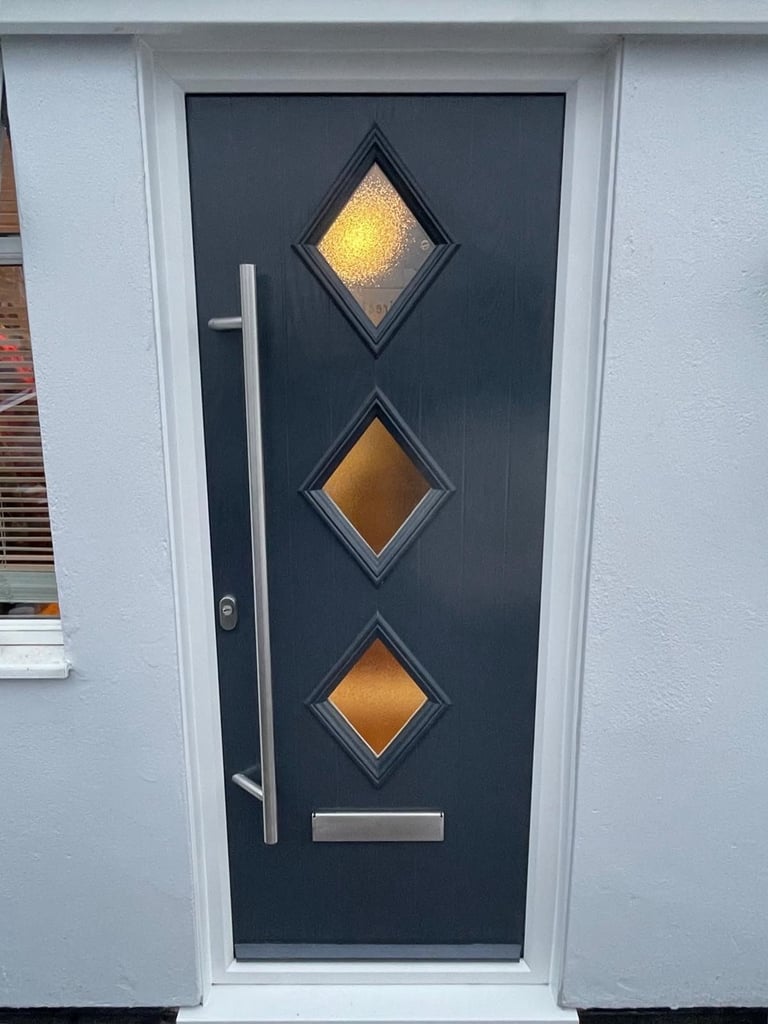 Modern black front door with white frame, three diamond-shaped amber glass panels, and stainless steel handle