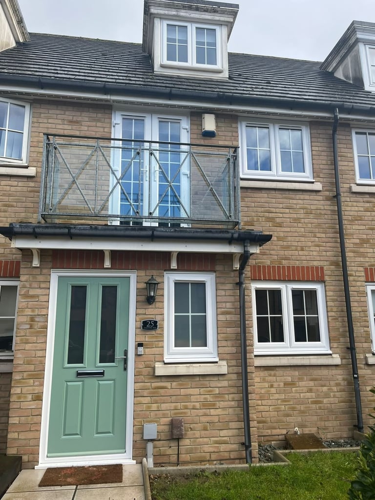 Brick townhouse with sage green door, multiple windows, metal balcony, and slate roof